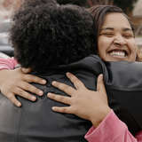 A smiling young woman hugs her mentor